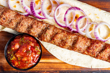 Delicious kebab wrap with fresh onions and tangy salsa served on a wooden platter