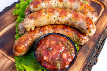 Grilled sausages served on a wooden platter with fresh lettuce and spicy salsa in a bowl