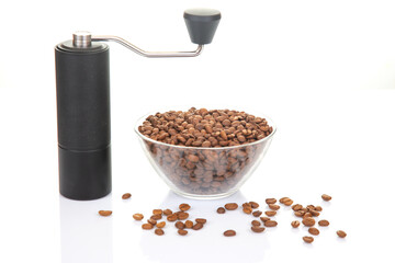 A stylish black manual coffee grinder paired with a glass bowl of freshly roasted coffee beans, some spilled around, set against a clean white backdrop for a minimalist look