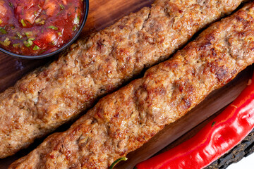 Grilled kebabs served with spicy sauce and fresh chili peppers on a wooden platter