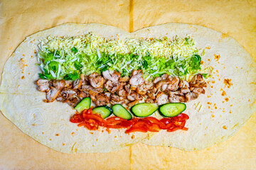 Colorful tortilla wrap filled with chicken, fresh vegetables, and cheese ready to be rolled