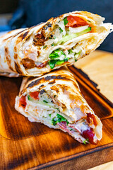 Delicious wrap with grilled chicken, fresh vegetables, and savory sauce on a wooden board in a rustic setting