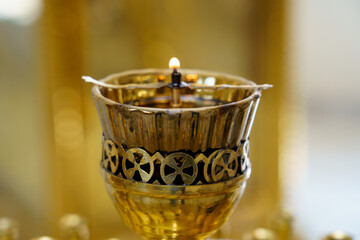 Candle burning in ornate holder during a religious ceremony in a temple setting with golden decorations