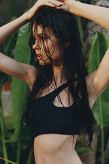 Beautiful woman in black bikini top posing confidently in front of palm tree with hands on head