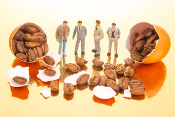 A creative scene featuring miniature figures in suits and casual attire standing near cracked orange eggs filled with coffee beans on a reflective golden surface.