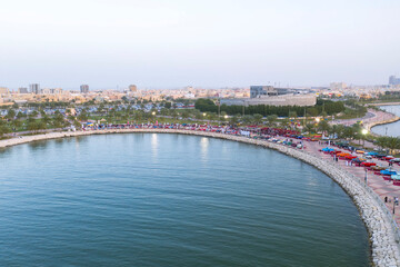 Obraz premium A distant aerial shot from the water of the antique autos lined along the promenade at the classic car show on the waterfront of Dammam, with the city of Dammam in the background