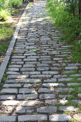 Footpath in the park with old paving stone. Ancient sidewalk made with old brick. Cobblestone in the city and industry of construction. Grass between paving stone.