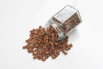 roasted coffee beans poured out of a glass transparent jar on a white background. kitchen utensils for coffee.