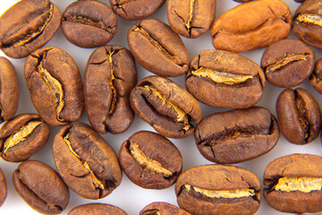 Macro shot of whole roasted coffee beans, highlighting their glossy finish and deep brown tones against a clean white backdrop. Ideal for food and beverage visuals.