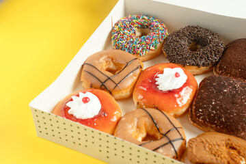 A variety of colorful donuts arranged in a box, featuring a mix of glazed, chocolate-coated, and...