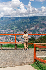 Young Colombian boy standing alone at mountain viewpoint overlooking Medellin.