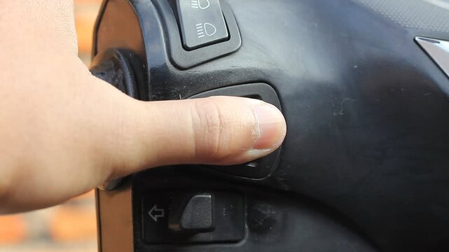A man's hand presses the motorbike horn repeatedly to reduce noise