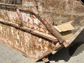 An old rusty dumpster sitting on a bustling city street filled with urban life and debris. The...