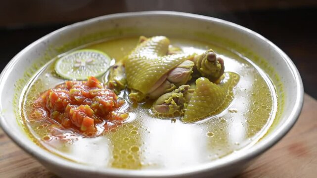  A vibrant chicken soto dish with herbs and vegetables, served hot in a metallic bowl with Indonesian sambal .