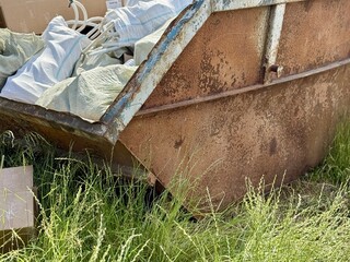 An Old and Rusty Dump Container That is Surrounded by Lush, Overgrown Grass and Weeds. A weathered...