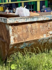 An Old and Rusty Dump Container That is Surrounded by Lush, Overgrown Grass and Weeds. A weathered...