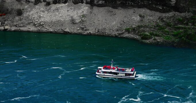 Rocky shoreline below Niagara Falls cascade revealing cliff face and swirling water, rocky shoreline below misty falls with foamy currents lapping edge, rocky shoreline below powerful waterfall