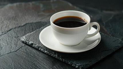 Fototapeta premium White coffee cup with saucer sits elegantly on black slate table, showcasing rich, dark brew. contrast creates sophisticated and inviting atmosphere for coffee lovers
