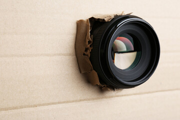 Hidden camera lens through hole in cardboard, closeup. Space for text