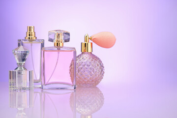 Bottles of perfume on mirror surface against violet gradient background, space for text