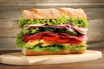 Tasty baguette sandwich with ham and vegetables on wooden table, closeup
