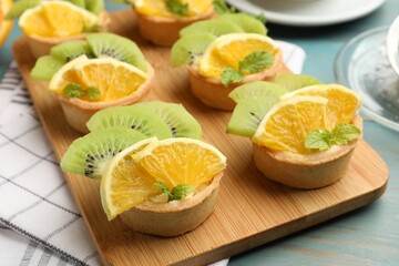 Tartlets with fruits and mint on light blue wooden table, closeup. Delicious dessert