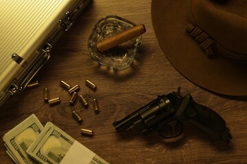 Mafia and criminal world. Gun, bullets, ashtray with cigar, hat, money and briefcase on wooden...
