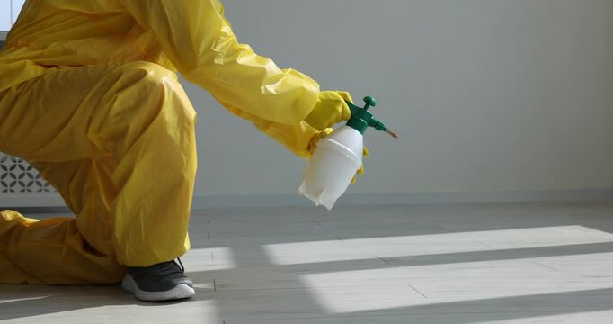 Pest control worker in protective suit spraying insecticide indoors, closeup