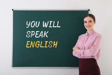 Teacher near green chalkboard with text You Will Speak English. Language course