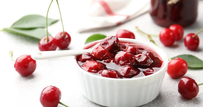 Tasty cherry jam and fresh fruits on light table, spinning