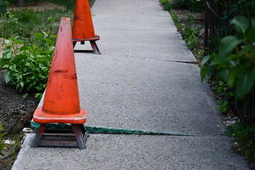 Damaged sidewalk. Safety cones on metal brackets.