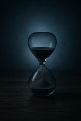 An Hourglass Placed on A Dark Wooden Surface. The Background is A Soft, Gradient Blue. The Hourglass is Partially Filled with Dark Sand, And the Lighting Creates A Moody And Contemplative Atmosphere.