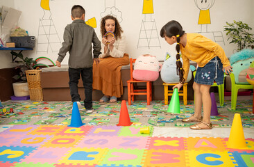 Preschool teacher and Hispanic children happily playing with colorful toy cones and matching hoops in a kindergarten classroom. Concept of color learning, school activity, and joyful educational play