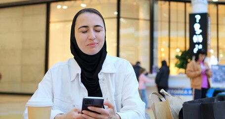 Young woman engaging with smartphone while enjoying coffee in trendy cafe, embodying modern digital...