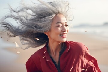 Asian woman with gray hair laughing joyfully on a sunny beach. Happy mature female enjoying retirement travel.