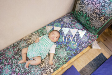 A 100-day-old Japanese baby lies comfortably on a vibrant, colorful sofa, with festive decorations...