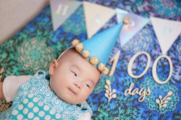 A 100-day-old Japanese baby lies comfortably on a vibrant, colorful sofa, with festive decorations...