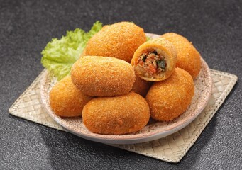 Kroket kentang. Croquettes are lumps of finely mashed potatoes filled with seasoned minced meat and mixed with vegetables such as carrots or green beans. The croquettes are coated with beaten egg and 
