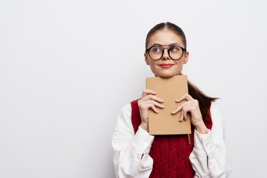 young woman holding a notebook, smiling, casual attire, glasses, studio shot, white background, text concept, happiness, creativity, inspiration