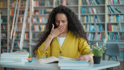 Indian Hispanic woman girl student teacher reading book textbook yawning tired library high school...