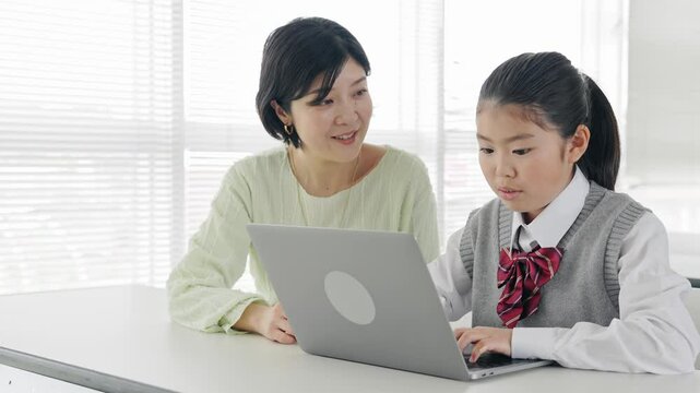 A girl learning how to use a computer from a female teacher in a classroom