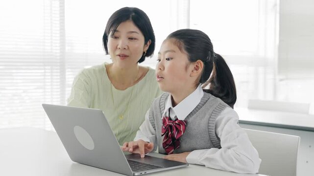 教室で女性教員からパソコンを教わる女の子