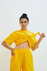 Young woman wearing a bright yellow outfit with a tied shirt and shorts poses confidently against a...
