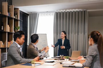 Young female speaker standing near flipchart with graphs diagrams, presenting market research results to focused diverse colleagues at brainstorming meeting or educational seminar in office.