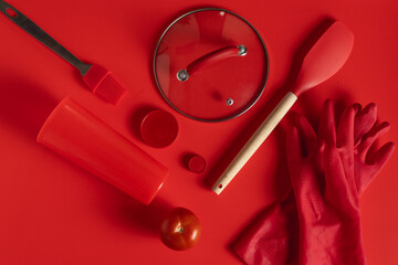 Red kitchen utensils, tomato and gloves lying on red background