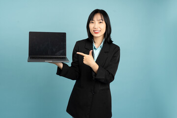 Young Asian professional presenting a laptop against a blue background in a studio environment...