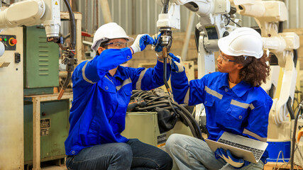 Male and femal engineers checking or maintenance electronic in AI or artificial intelligence Robot, robot arm in the manufacturing automation and robotics manufacture room. Service technical engineer.