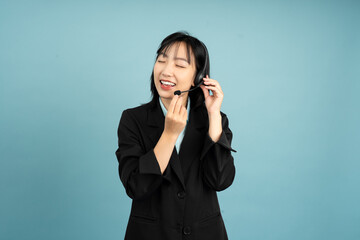 Smiling Asian woman in a black blazer using a headset while engaging in a conversation against a...