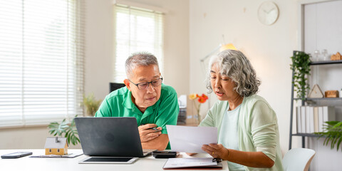 Senior old couple holding documents reading paper bills paying bank loan online, calculating...