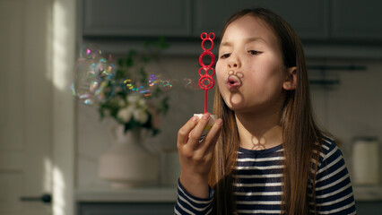 Little girl blowing soap bubbles childhood playful child daughter kid home air joy playing soapy...